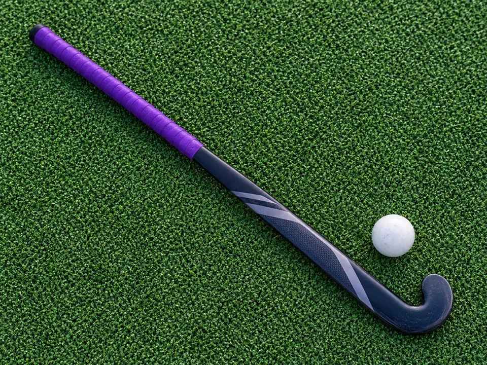 Field hockey stick with a purple grip and a white ball on artificial turf